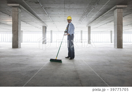 Asian businessman cleaning up with a broom in a large empty raw office space. 39775705