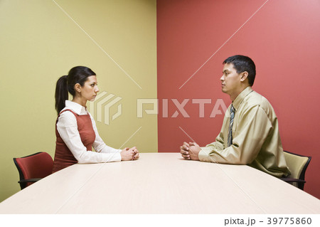 Businessman and woman sitting on opposite sides of a conference table in a very colourful room. 39775860