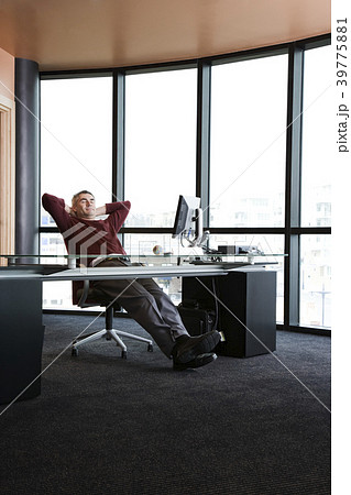 Casually dressed Caucasian businessman relaxed at his desk in front of a large bank of windows. Casually dressed Caucasian businessman relaxed at his desk in front of a large bank of windows. 39775881