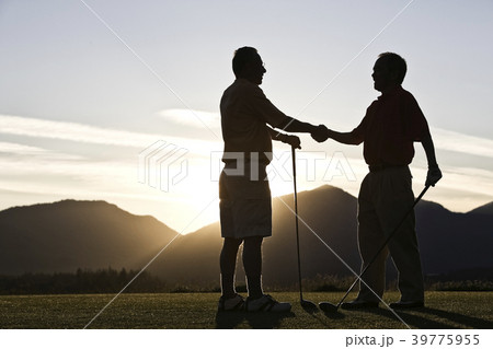 Two senior friends approach the first tee of a golf course at sunrise. 39775955
