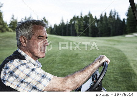 Senior golfer driving a golf cart on the cart path of a golf course. 39776014