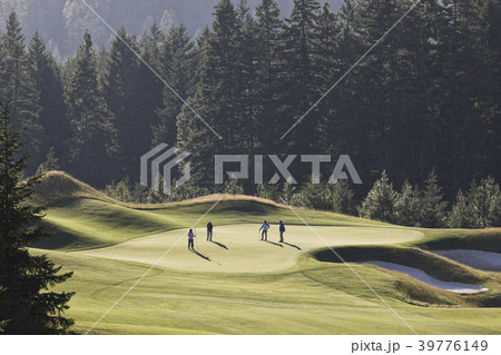 View from above of four golfers playing golf on a green in the distance. View from above of four golfers playing golf on a green in the distance. 39776149