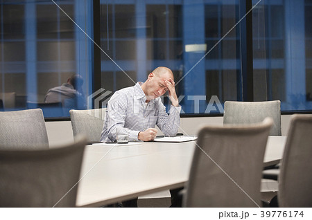 A Caucasian businessman under stress while working at night at a conference table. 39776174