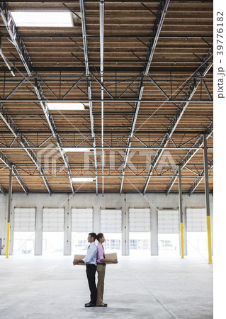 Caucasian man and black female holding cardboard boxes in middle of empty warehouse interior. Caucasian man and black female holding cardboard boxes in middle of empty warehouse interior. 39776182