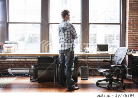 Caucasian man standing near a bank of windows at his creative office workstation. Caucasian man standing near a bank of windows at his creative office workstation. 39776394