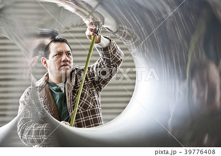 Hispanic man factory worker measuring diameter of pipe in a sheet metal factory. 39776408