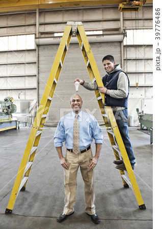 Black man factory owner and young Caucasian man factory worker goofing off together on the floor of a sheet metal factory. 39776486