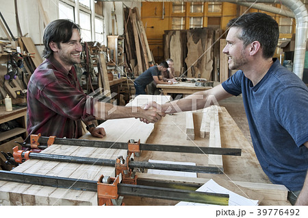 Team of four men, factory workers at a work station in a large woodworking factory, two shaking hands. 39776492