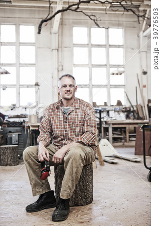 Caucasian man factory worker sitting on a stool in a woodworking factory. Caucasian man factory worker sitting on a stool in a woodworking factory. 39776503