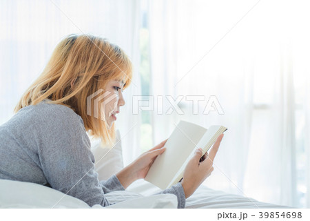 Woman enjoying lying on the bed reading book. 39854698