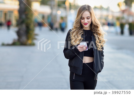 Blonde woman texting with her smartphone in urban background Blonde woman texting with her smartphone in urban background 39927550