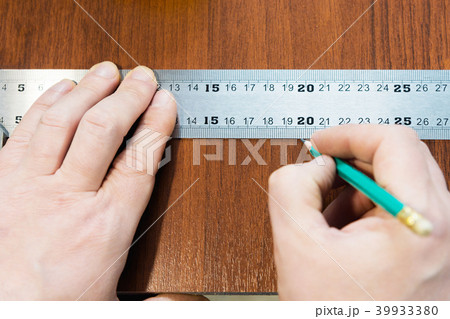 Close-up Men's hands draw a pencil on the ruler with a sub-standard template for cutting out Close-up Men's hands draw a pencil on the ruler with a sub-standard template for cutting out 39933380
