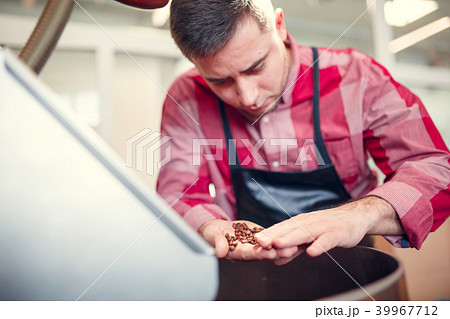 Image of young businessman with coffee beans in hand next to roaster Image of young businessman with coffee beans in hand next to roaster 39967712