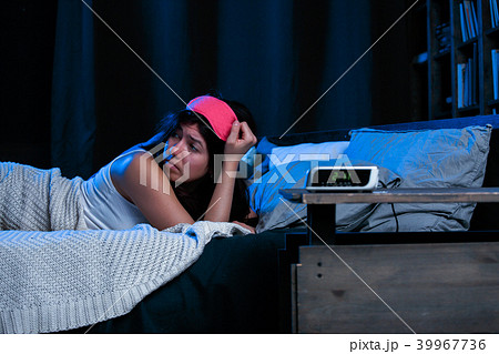 Image of young brunette with insomnia with pink eye patch lying on bed next to clock Image of young brunette with insomnia with pink eye patch lying on bed next to clock 39967736