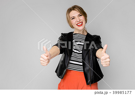 Attractive young blonde girl in striped blouse and leather jacket smiling laughing with thumbs up 39985177
