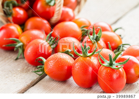 Small red cherry tomatoes spill out of a  basket. 39989867