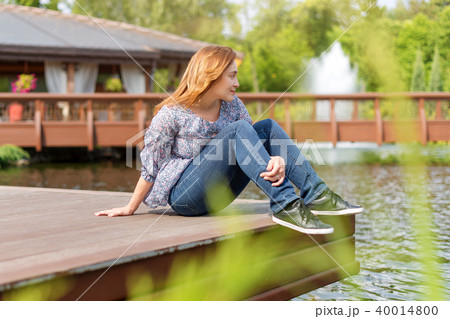 Young woman resting and having fun in the park sitting on a pier over the lake. 40014800