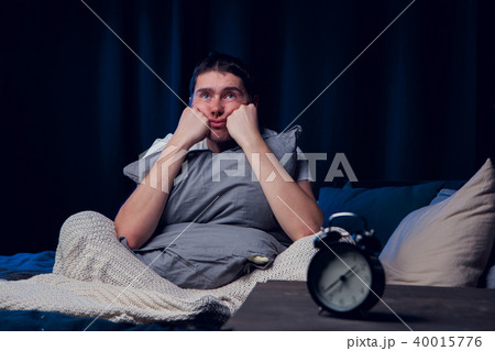 Image of brunet with insomnia with pillow sitting next to alarm 40015776