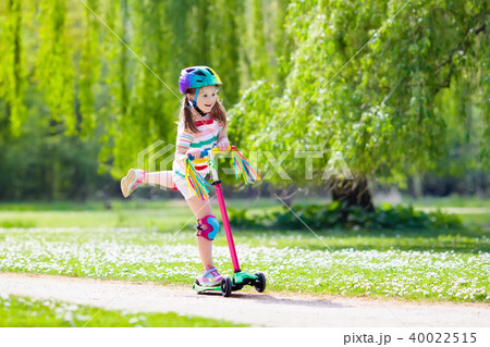 Child riding kick scooter in summer park. 40022515