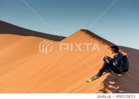 male photographer sitting on sand dune, Namibia 40023655