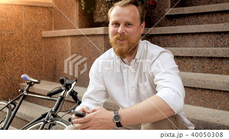 Portrait of smiling stylish man sitting on stone stairs next to vintage bicycle Portrait of smiling stylish man sitting on stone stairs next to vintage bicycle 40050308