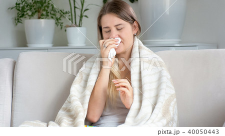Portrait of sick young woman covered in blanket sneezing in tissues 40050443