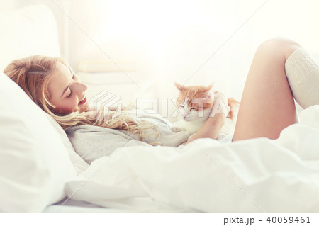 happy young woman with cat in bed at home 40059461