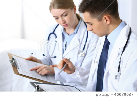 Doctors writing papers using clipboard. Physicians discussing medication program or studying at Doctors writing papers using clipboard. Physicians discussing medication program or studying at 40079037