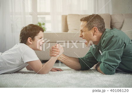 Cheerful father and son playing arm-wrestling at home Cheerful father and son playing arm-wrestling at home 40106120