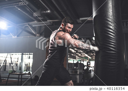 Male boxer training with punching bag in dark sports hall. Male boxer training with punching bag in dark sports hall. 40116354