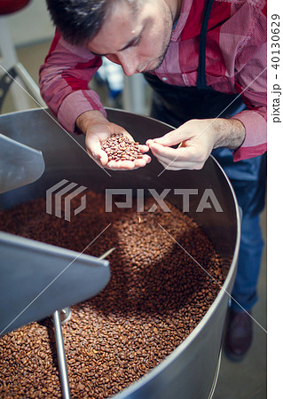 Image of young man with coffee beans in hand next to roaster Image of young man with coffee beans in hand next to roaster 40130629