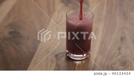 closeup pour red berry drink into a glass on wood table 40133434