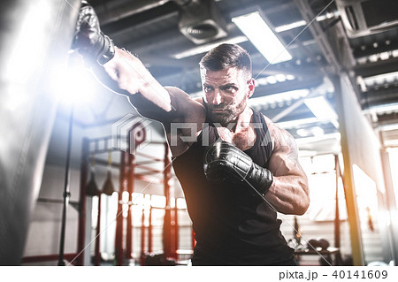 Male boxer training with punching bag in dark sports hall. 40141609