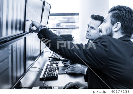 Stock traders looking at market data on computer screens. 40177158
