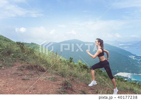 Slender young female athlete doing cardio exercise going up the mountain with sea in background. Slender young female athlete doing cardio exercise going up the mountain with sea in background. 40177238