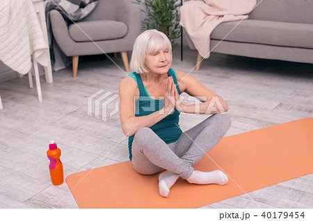 Pleasant senior woman meditating at living room Pleasant senior woman meditating at living room 40179454