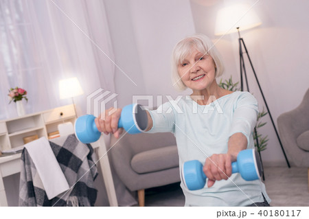 Happy elderly woman exercising with blue dumbbells 40180117