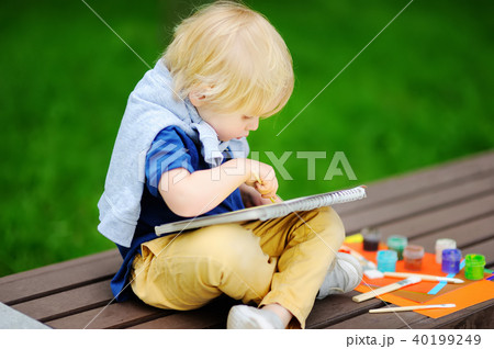 Cute little boy drawing with colorful paints in summer park Cute little boy drawing with colorful paints in summer park 40199249