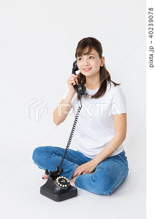 あぐらをかいて黒電話をかける女性の写真素材