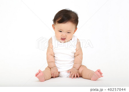 白バックの前に一人座り遊ぶ女の子の赤ちゃんの写真素材