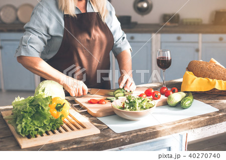 Senior woman chopping cucumber for salad in kitchen Senior woman chopping cucumber for salad in kitchen 40270740