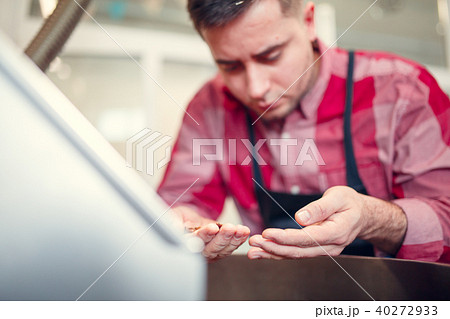 Photo of young man holding roasted coffee beans near industrial coffee grinder 40272933