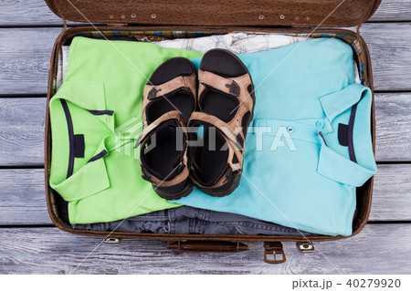 Suitcase with folded male clothes and pair of sandals. 40279920