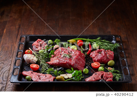 Flat lay of raw beefsteak with vegetables, herbs and spicies on metal tray, close-up, selective 40290412