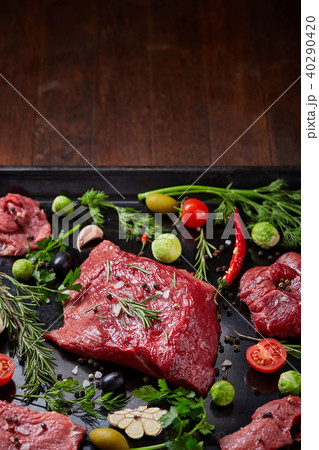 Flat lay of raw beefsteak with vegetables, herbs and spicies on metal tray, close-up, selective 40290420