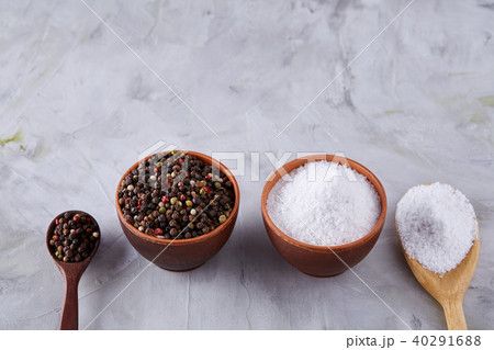 Conceptual composition of salt and pepper on spoons and bowls over light background, top view, close 40291688