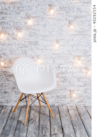 Modern white plastic chair in loft white room interior with wooden floor. Light bulbs garland on 40292554