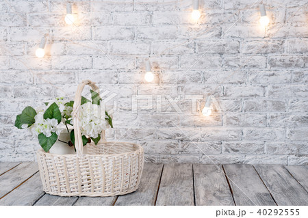 Flowers in basket with light bulbs on white brick background with wooden floor. 40292555