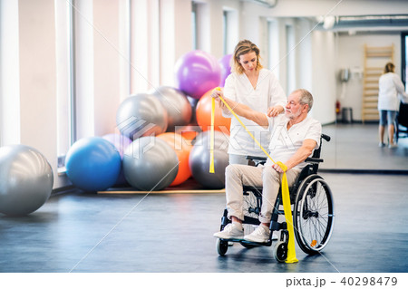 Young woman physiotherapist working with a senior man in wheelchair. 40298479