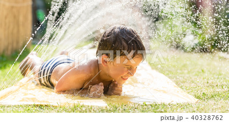 Boy cooling down with garden hose, family in the background Boy cooling down with garden hose, family in the background 40328762